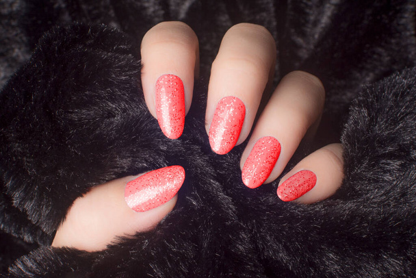 Female hand with glittered red nails is holding black fur, manicure and nail care concept. - Photo, Image