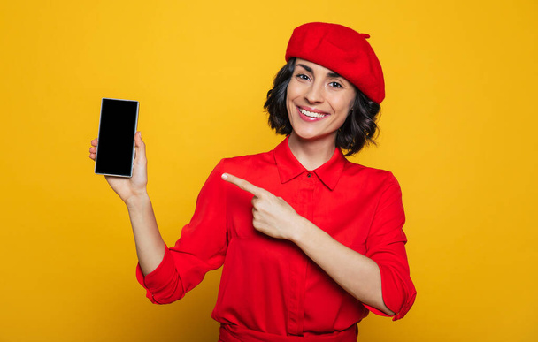 An attractive french woman, dressed in a parisian style, with a red beret, points on her smartphone. - Photo, image
