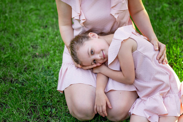 mother and daughter 5-6 years old walk in the Park in the summer, the daughter lies on her mother's lap on a bench, the concept of a happy family, the relationship of mother and child, mother's day - 写真・画像