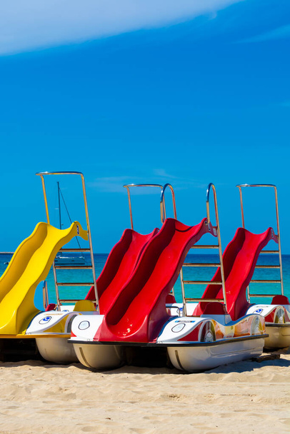 Színes pedálos csónak csúszdákkal kiadó a homokos tengerparton, kék tengervízzel - Fotó, kép