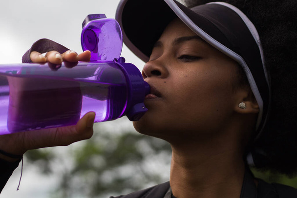 黒の飲料水に紫色のボトルで身を包んだ黒人女性 - 写真・画像