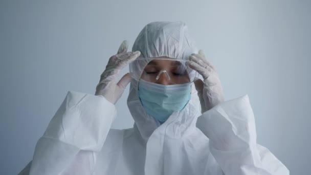 happy female doctor in protective suit enjoying end of working day during pandemic due to coronavirus on white background - Imágenes, Vídeo