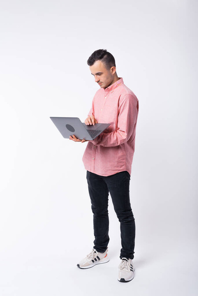 Full body photo of a young man using the laptop he is holding over white background - Fotó, kép