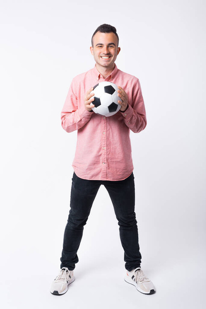 Happy young man is smiling at the camera while holding a soccer ball on white background - Fotografie, Obrázek