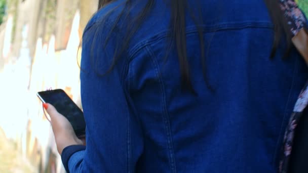 Csinos kaukázusi lány fülhallgatóval és okostelefonnal a kamera előtt. Kültéri fal graffitivel a háttérben. 4k, lassított mozgás 75fps - Felvétel, videó