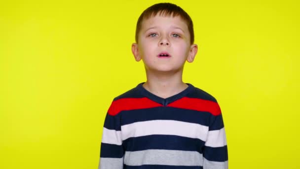 Μικρό παιδί αγόρι σε πολύχρωμο πουλόβερ στέκεται σε κίτρινο φόντο με χώρο αντίγραφο - Πλάνα, βίντεο