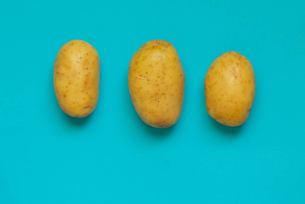 three raw young potatoes on a blue background - Photo, Image
