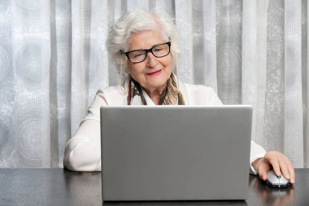 old lady with glasses looking at a computer on a wooden table. concept of technology , grandma, health - Foto, Bild