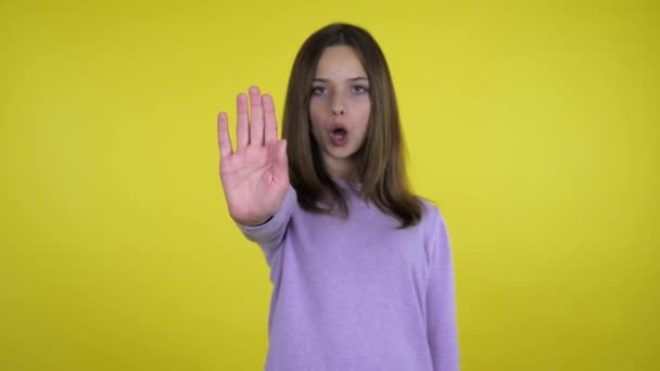 Tiener meisje heft haar hand met een palm en zegt stop op gele achtergrond - Video