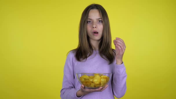 Nastoletnia dziewczyna je chipsy ziemniaczane ze szklaną miską i jest niezadowolona ze smaku - Materiał filmowy, wideo
