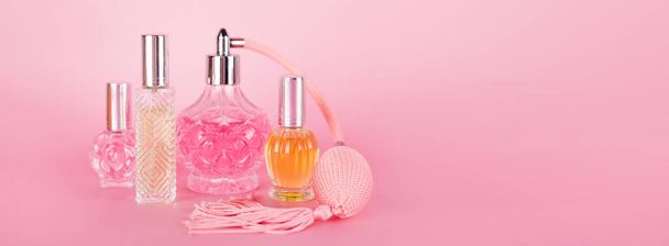 Different transparent perfume bottles on pink background. Aromatic essence bottles. Perfumery, cosmetics, fragrance collection. Banner, free space for text - Photo, Image