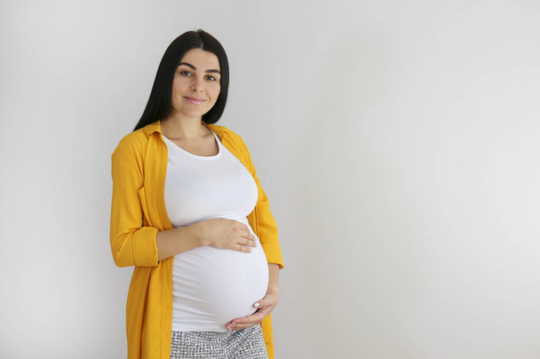 Portrait shot of young beautiful woman on third trimester of pregnancy. Close up of pregnant female with arms on her round belly. Expecting a child concept. Background, copy space. - Fotografie, Obrázek
