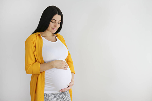 Portrait shot of young beautiful woman on third trimester of pregnancy. Close up of pregnant female with arms on her round belly. Expecting a child concept. Background, copy space. - Zdjęcie, obraz