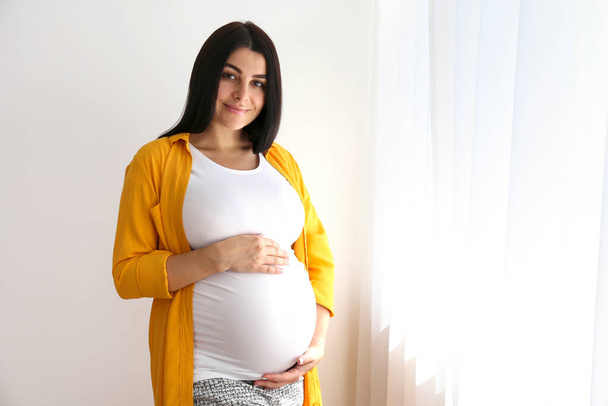 Portrait shot of young beautiful woman on third trimester of pregnancy. Close up of pregnant female with arms on her round belly. Expecting a child concept. Background, copy space. - Valokuva, kuva