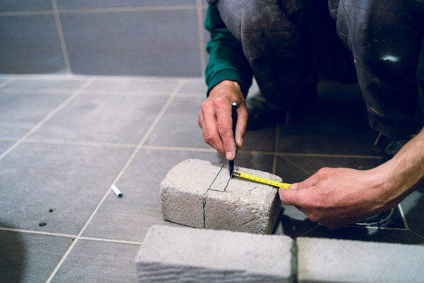 Τεχνίτης οικοδομών που μετρά το υλικό από τούβλα τσιμέντου στο μπάνιο της πολυκατοικίας μέτρηση κτιρίου χρησιμοποιώντας στυλό για να κάνει ένα σήμα - Φωτογραφία, εικόνα