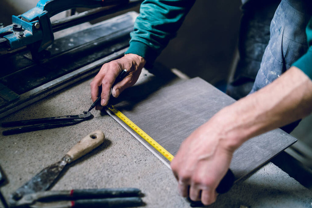 Detailní informace o stavební dělník řemeslník pomocí nástroje pro řezání keramických dlaždic pro pokládání instalace do koupelny dělat měření značky pomocí měřicí pásky a pera - Fotografie, Obrázek