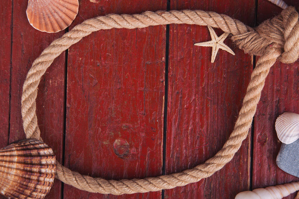 Nautical knots with rope and seashell on old red wooden board with place for text. The style of old pirate ships. Wooden background with starfish and marine rope. - Photo, Image