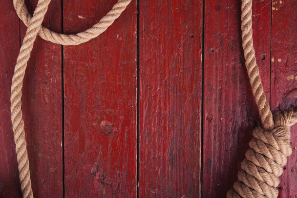 木製ボード上のロープ結び目。テキストのための場所と古い赤い木製のボード上の航海ノット。海洋ロープ付きの木の背景. - 写真・画像
