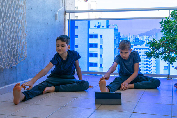 Jongens met tablet computer die sport oefeningen doen op het balkon. Sport, gezonde levensstijl, actieve vrije tijd thuis - Foto, afbeelding