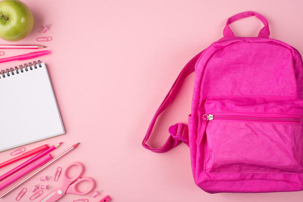 Сверху над головой фотография розового рюкзака зеленое яблоко и красочные канцелярские принадлежности изолированы на пастельно-розовом фоне
 - Фото, изображение