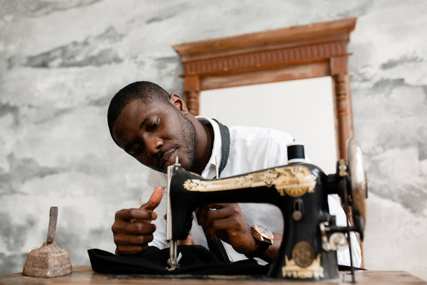 Portrait of a black man seamstress sewing himself a black suit to demonstrate at the exhibition of his work in the studio - Фото, зображення