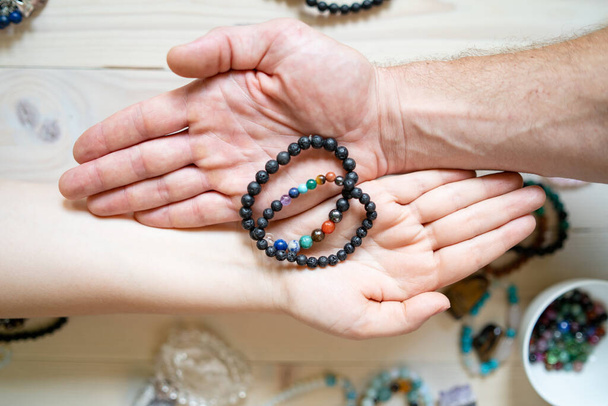 Vista de alto ângulo em mãos masculinas e femininas segurando jóias de cristal pulseiras feitas à mão para a sorte do amor e charme energia de cura
 - Foto, Imagem