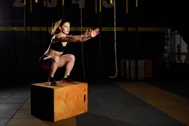 Athletic woman in sportswear jumping on crossfit box in fitness gym - Valokuva, kuva