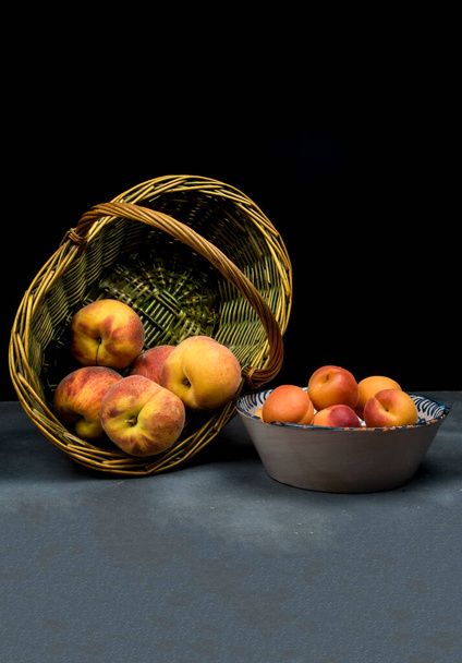 abricots sur plat en céramique et pêches sur panier en osier - Photo, image