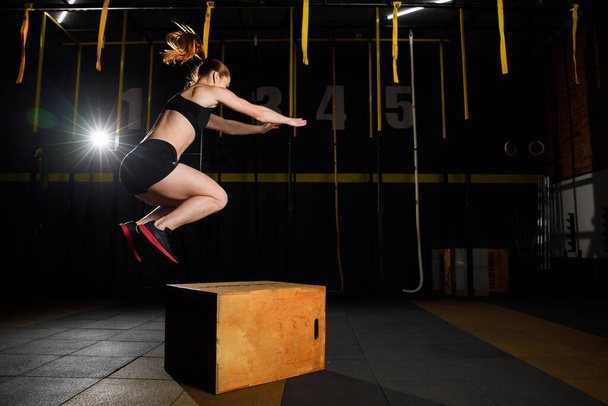 Athletic woman in sportswear jumping on crossfit box in fitness gym - Photo, image