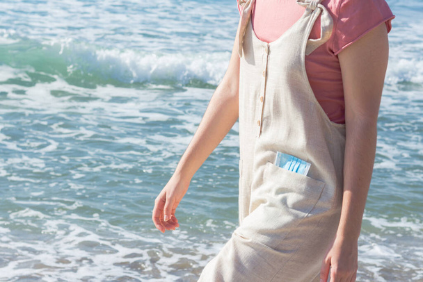 A girl with a mask in her pocket walking on the beach with the sea in the background on a sunny day - Foto, Bild