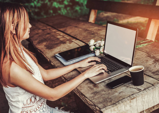 コーヒーカップ、イチゴ、牡丹の花の花束、スマートフォンと大まかな木製のテーブルでラップトップコンピュータを使用して入力する若い女性。屋外公園で働いているフリーランス。トーニング - 写真・画像