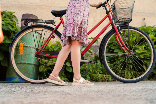 Gros plan sur les jambes de la femme femelle debout à côté du vélo portant une robe d'été dans une journée ensoleillée - Photo, image