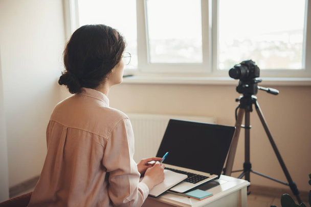 Jovem senhora ter aulas on-line é usar uma câmera e laptop enquanto vestindo óculos e discutir durante a reunião
 - Foto, Imagem