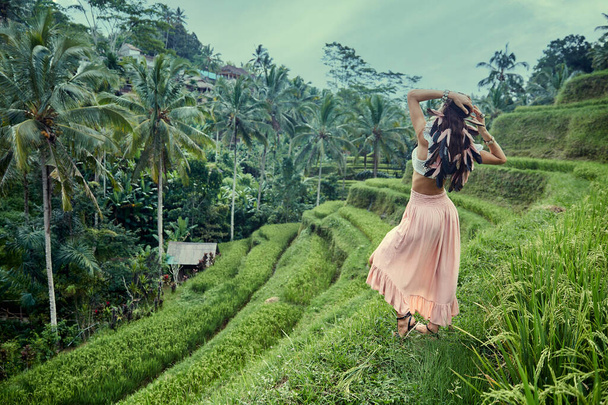 Bella ragazza in un abito rosa con le piume nei capelli su una terrazza di riso, Bali
 - Foto, immagini