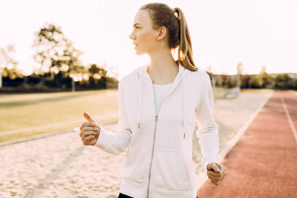 Mujer joven atlética en ropa deportiva corriendo alrededor del estadio al amanecer
 - Foto, Imagen