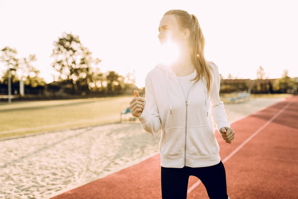 Athletic young woman in sportswear running around the stadium at dawn - Photo, Image
