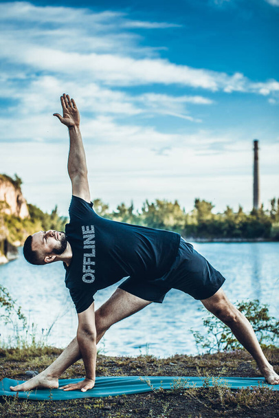 Sporty bearded man doing arm balance on rocky seashore. International Day of Yoga on quarry lake. - Photo, Image