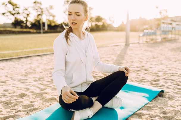 sporty woman practices yoga and meditation in the Lotus position while sitting on a fitness Mat on the beach in the morning - Foto, Imagen