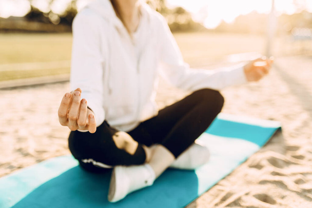 sporty woman practices yoga and meditation in the Lotus position while sitting on a fitness Mat on the beach in the morning - Photo, image