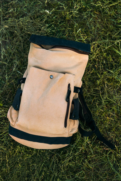 Gros plan d'une main beige touristique avec un sac à dos noir se trouve sur une prairie d'herbe verte.  - Photo, image