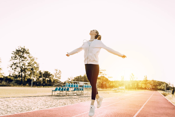 Fitness woman doing cardio interval training outdoors. A girl in sports clothes trains jumps against the background of the dawn - 写真・画像
