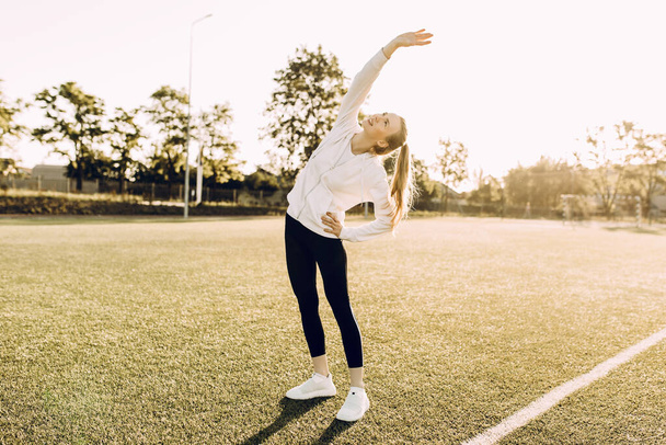 Attractive slim athletic woman doing stretching exercises in the open air. Sports, coronavirus, quarantine - Photo, image