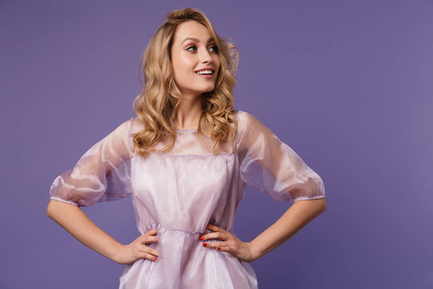 Image of joyful caucasian woman smiling and holding hands on her waist isolated over purple background - Foto, Imagem