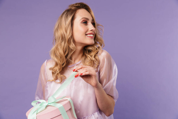 Image of cheerful caucasian woman smiling and opening gift box isolated over purple background - Fotó, kép