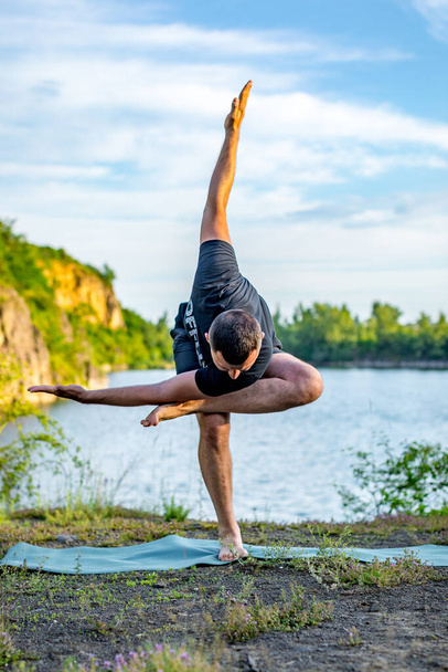 A good looking young bearded man doing yoga on quarry lake backdrop. International Day of Yoga concept. - Photo, Image