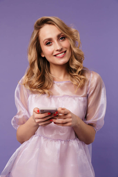 Bild einer glücklichen jungen Frau, die auf dem Smartphone lächelt und auf lila Hintergrund tippt - Foto, Bild