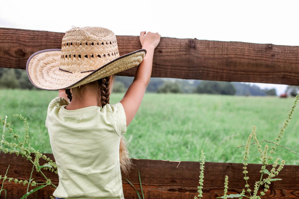 Yerel tatil, güvende kal, evde kal. Kovboy şapkalı küçük kız dağların arasındaki çiftlikte oynuyor, kırsalda mutlu bir yaz, çocukluk ve hayaller - Fotoğraf, Görsel