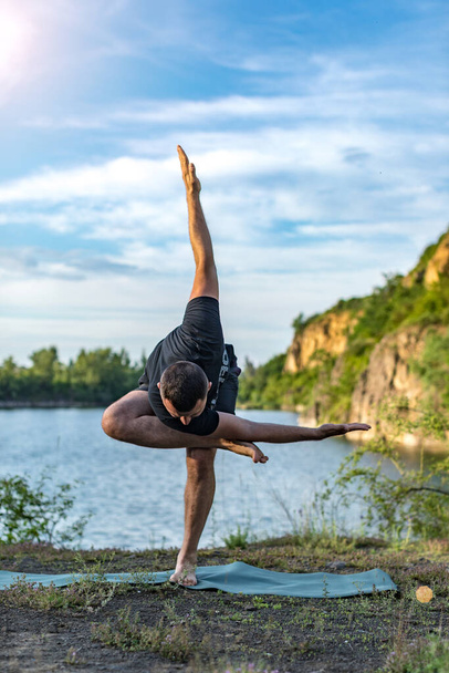 Un joven barbudo bien parecido haciendo yoga en el fondo de la cantera del lago. Concepto del Día Internacional del Yoga. - Foto, Imagen