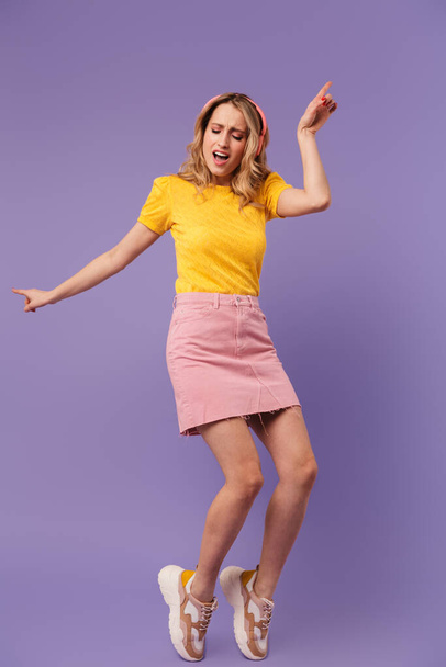 Image of nice happy woman dancing and singing while using headphones isolated over purple background - Foto, Imagem