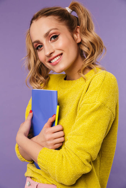 Kuva hymyilevä kaunis nainen kaksi häntää poseeraa harjoituskirjan ja lyijykynä eristetty violetti tausta - Valokuva, kuva